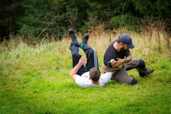 Zwei Personen im Bodenkampf auf einer Wiese, einer hält den anderen fest