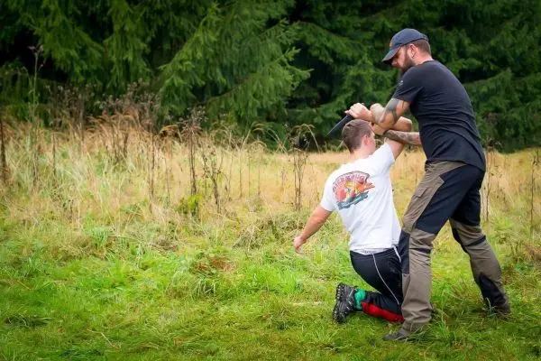 Zwei Personen in einer Wiese, eine Person kniet und wird von der anderen festgehalten