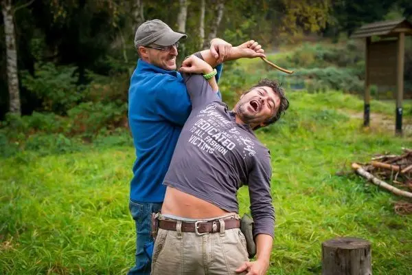 Zwei Personen interagieren im Freien, eine hält einen Stock und zieht den anderen zurück
