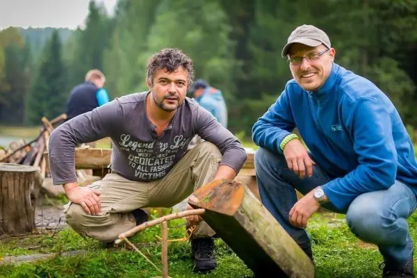 Zwei Personen knien neben einem Holzstück mit einer Kerbe im Wald