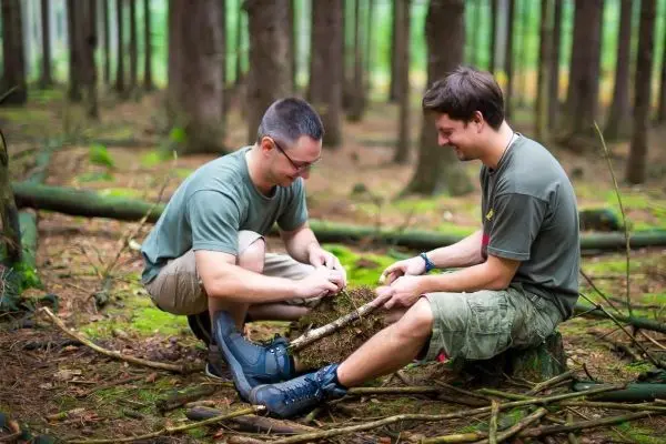Zwei Personen sitzen im Wald und bauen eine Feuerstelle