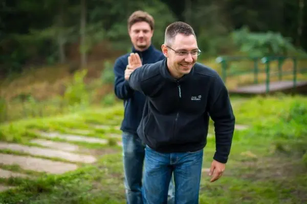 Zwei Personen stehen auf einer Wiese, eine Person berührt die andere von hinten