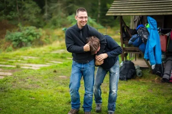 Zwei Personen stehen auf einer Wiese, eine Person hält die andere am Kopf