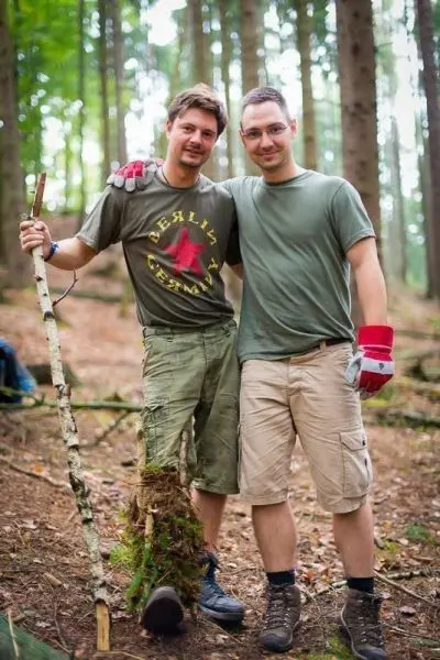 Zwei Personen stehen im Wald, einer hält einen Stock mit Moos