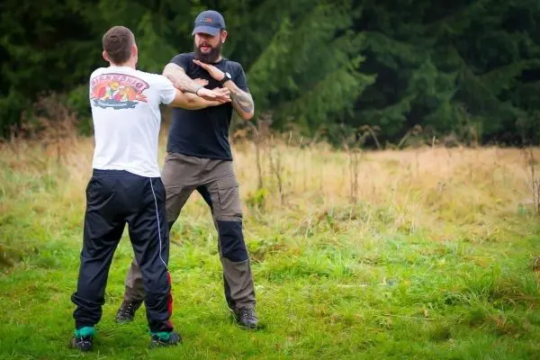 Zwei Personen üben eine Selbstverteidigungstechnik im Freien auf einer Wiese