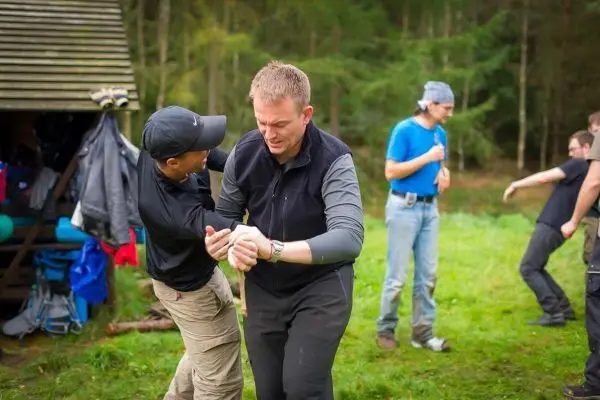 Zwei Personen üben eine Selbstverteidigungstechnik im Freien, während andere zuschauen