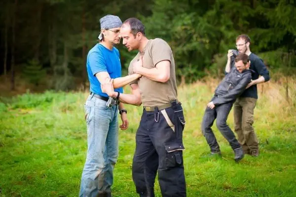 Zwei Personen üben eine Selbstverteidigungstechnik im Freien, während zwei weitere zuschauen