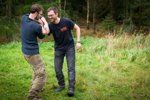 Zwei Personen üben eine Technik im Gras, einer hält den anderen am Arm