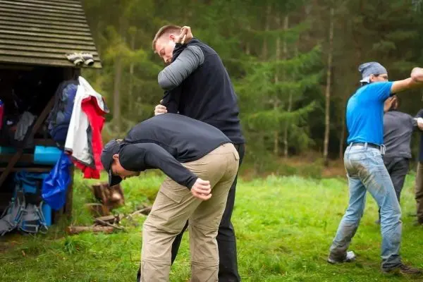 Zwei Personen üben eine Technik zur Kontrolle in einer Wiese nahe einer Hütte