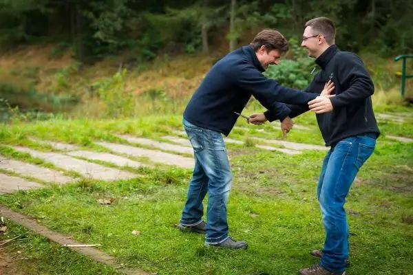 Zwei Personen üben eine Technik zur Selbstverteidigung auf einer Wiese