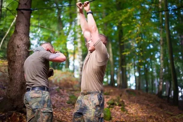 Zwei Personen überqueren eine selbstgebaute Seilbrücke im Wald
