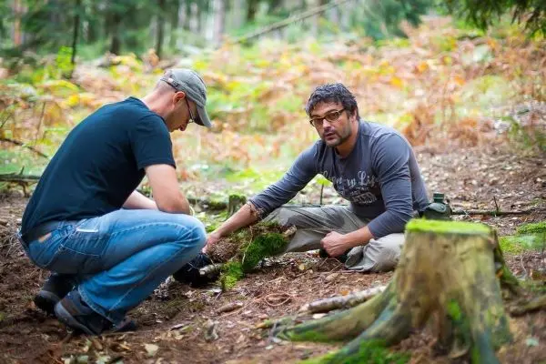 Zwei Personen untersuchen den Boden im Wald, einer greift nach Moos