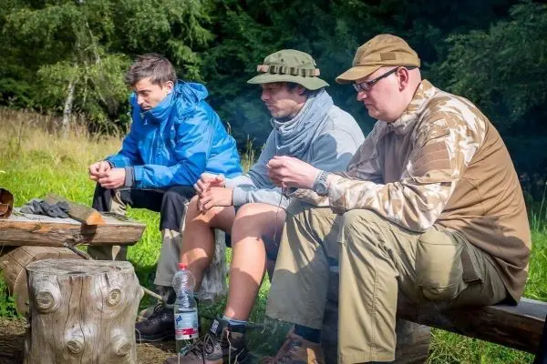Drei Personen sitzen an einem Holzstamm und schauen nach vorne
