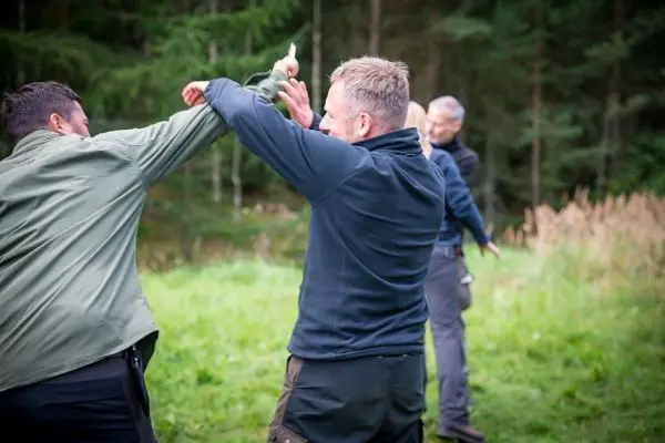 Drei Personen üben eine Selbstverteidigungstechnik im Freien