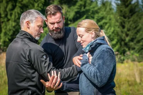 Drei Personen üben eine Technik zur Selbstverteidigung im Freien