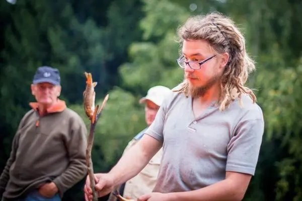 Ein Mann hält einen Stock mit gegrilltem Fisch über einer Feuerstelle