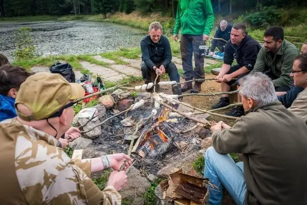 Gruppe sitzt um ein Feuer, während sie mit Stöcken Brot über den Flammen rösten