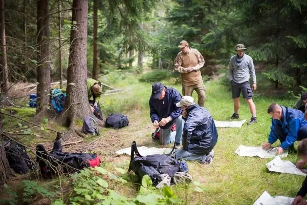 Gruppenteilnehmer analysieren Karten im Wald, Rucksäcke liegen auf dem Boden