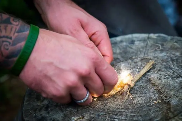 Hände erzeugen Funken auf trockenem Holzstück beim Feuer machen