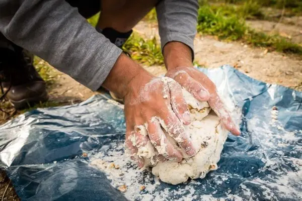 Hände kneten Teig auf einer blauen Plane im Freien