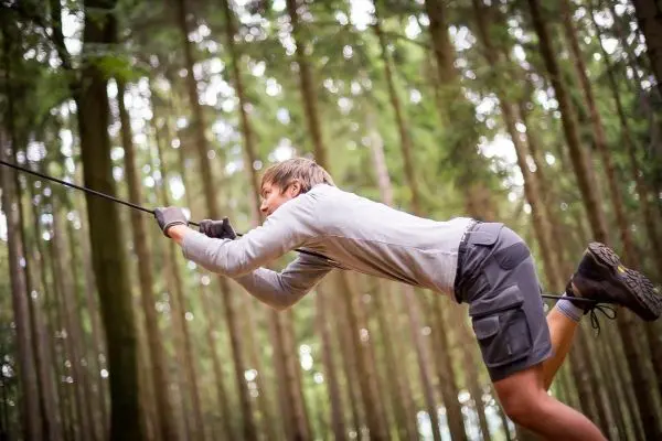 Junge überquert eine selbstgebaute Seilbrücke im Wald