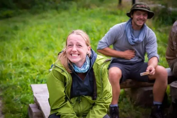 Lächelnde Person in grüner Jacke sitzt auf Holzbank im Freien
