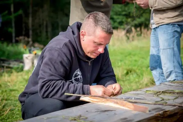 Mann bearbeitet Holzstück auf einem Tisch mit Schnur und Werkzeug