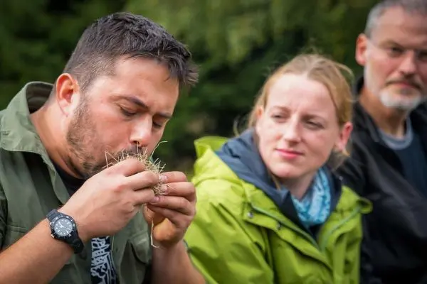 Mann bläst in Zundernest, während zwei Personen zuschauen