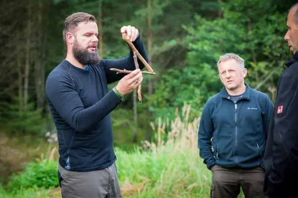 Mann demonstriert eine selbstgebaute Konstruktion aus Ästen für eine Falle