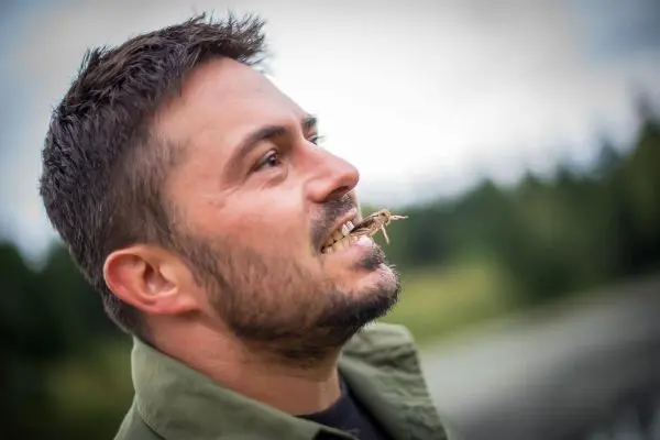 Mann hält eine Heuschrecke im Mund und schaut nach oben