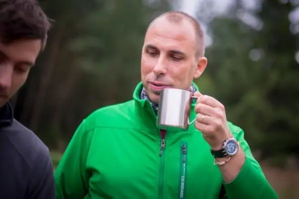 Mann in grüner Jacke hält einen Metallbecher und schaut nachdenklich