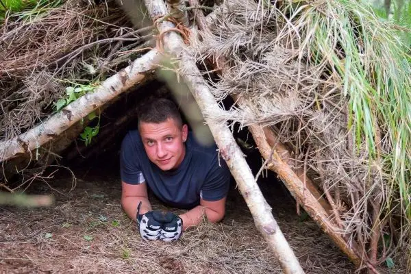 Mann in Tarp-Notunterkunft mit Handschuhen und Werkzeug in der Hand