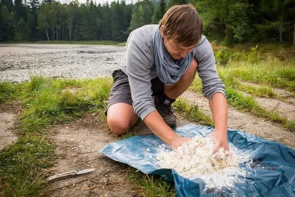 Mann knetet eine Mischung auf einer blauen Plane am Ufer eines Gewässers