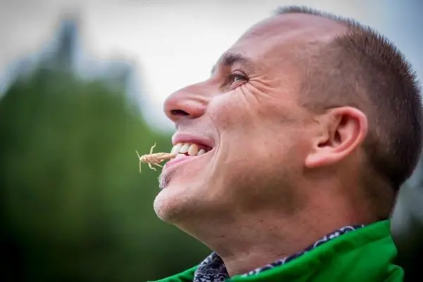 Mann mit Insekt im Mund lächelt in die Kamera