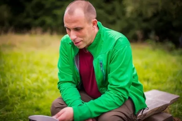 Mann sitzt auf Holzbank und betrachtet einen Kochtopf auf dem Boden