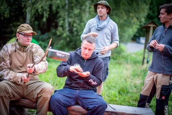 Mann sitzt auf Holzbank und hält ein kleines Objekt in der Hand, andere beobachten