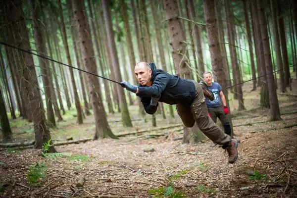 Mann überquert selbstgebaute Seilbrücke zwischen Bäumen im Wald
