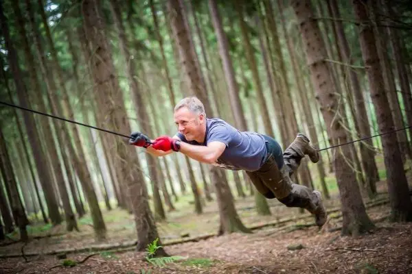 Mann überquert selbstgebaute Seilbrücke zwischen Bäumen im Wald