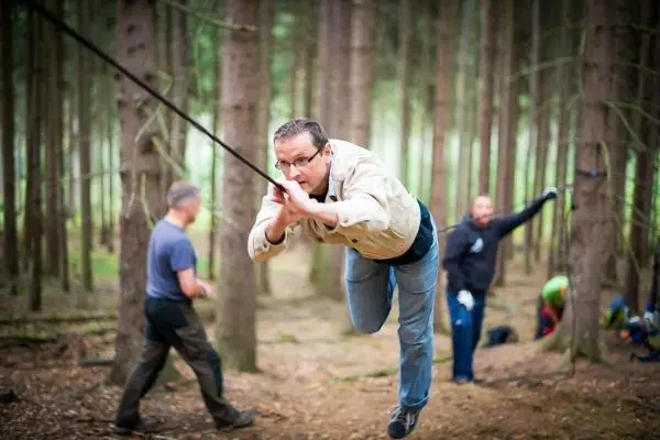 Mann überquert selbstgebaute Seilbrücke zwischen Bäumen im Wald