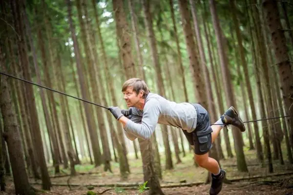 Mann überquert selbstgebaute Seilbrücke zwischen Bäumen im Wald