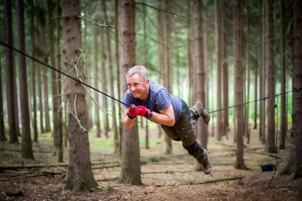 Mann überquert selbstgebaute Seilbrücke zwischen Bäumen im Wald