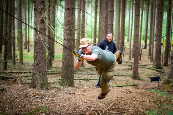 Mann überquert selbstgebaute Seilbrücke zwischen Bäumen im Wald