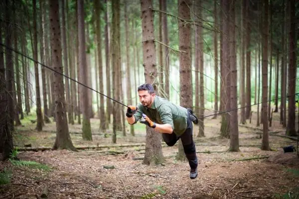 Mann überquert selbstgebaute Seilbrücke zwischen Bäumen im Wald
