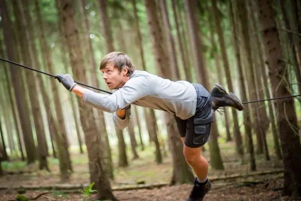 Mann überquert selbstgebaute Seilbrücke zwischen Bäumen im Wald