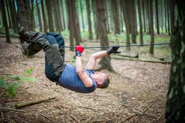Mann überquert selbstgebaute Seilbrücke zwischen zwei Bäumen im Wald