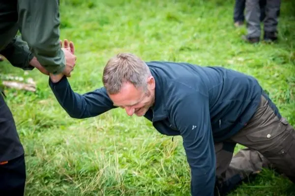 Mann wird von einer anderen Person am Arm hochgezogen, während er auf dem Boden kniet