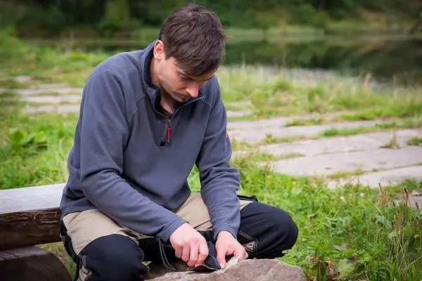 Messer schneidet Holzstück auf einem Stein am Ufer eines Gewässers