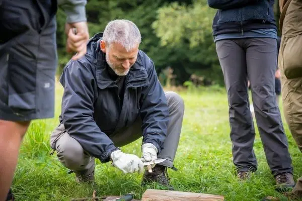 Messer schneidet Holzstück auf grünem Grasboden während einer praktischen Übung