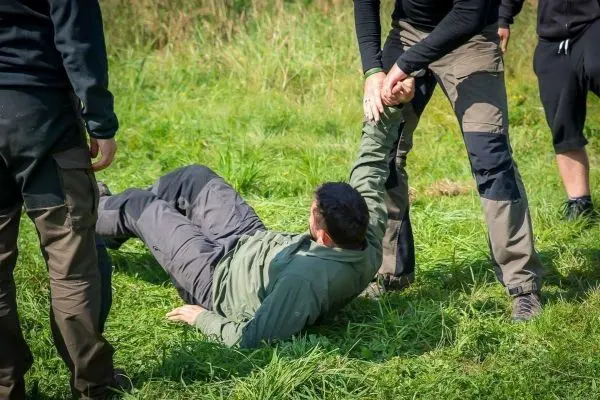 Person am Boden wird von zwei anderen Personen an den Armen gehalten