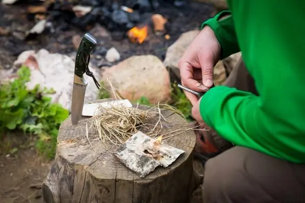 Person bereitet Feuerstelle mit Zunder und Messer vor beim Survival Training